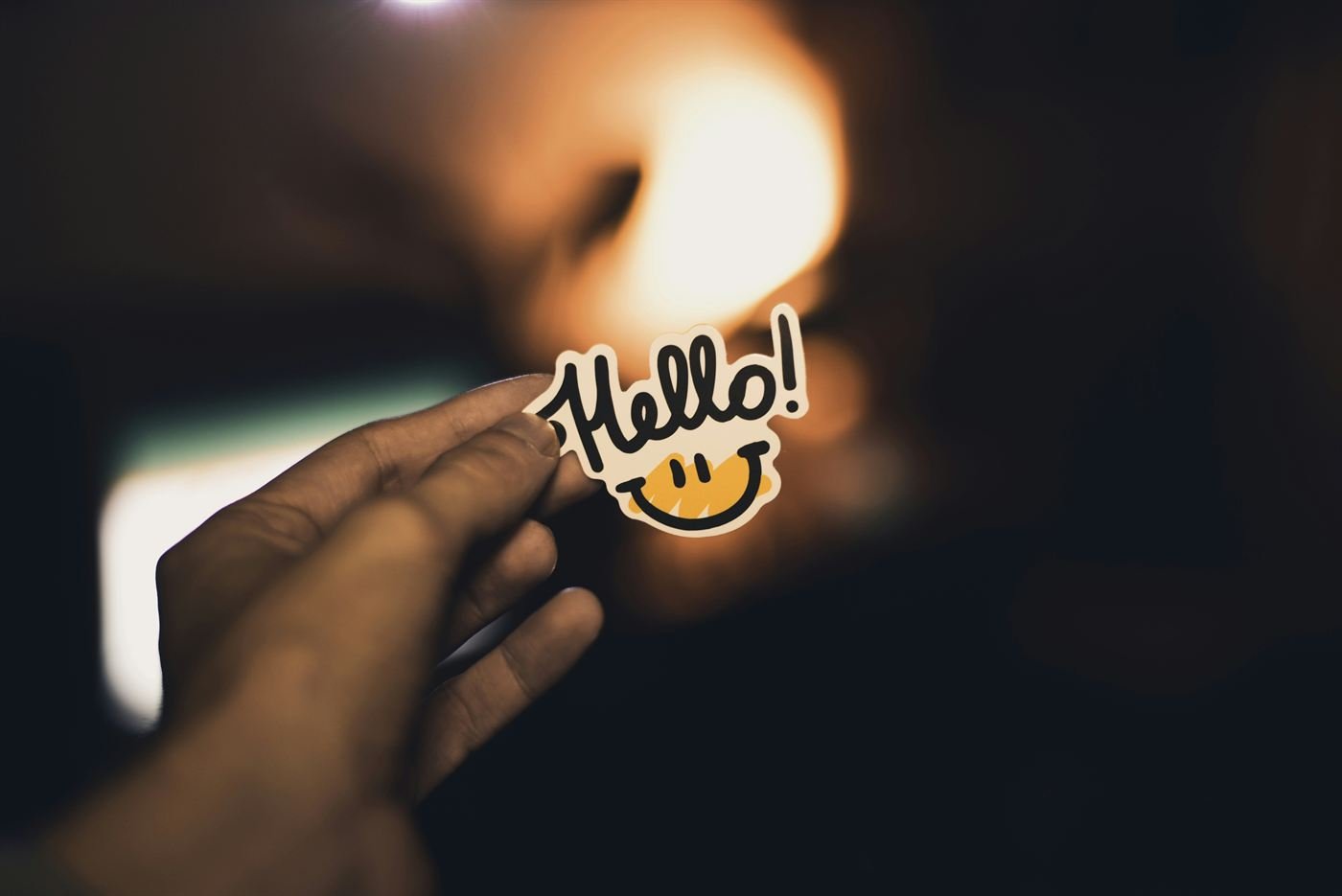 A hand holding a card that reads Hello, with a smiling face beneath it